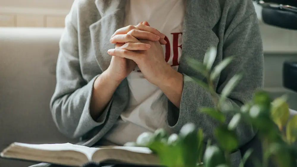 A Christian praying with the bible open. Photo by Signe Lightland on Unsplash.